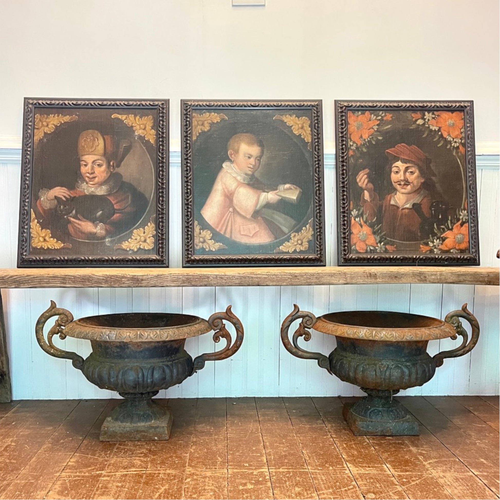 European Old Master style character portrait paintings displayed together above antique cast iron garden urns.