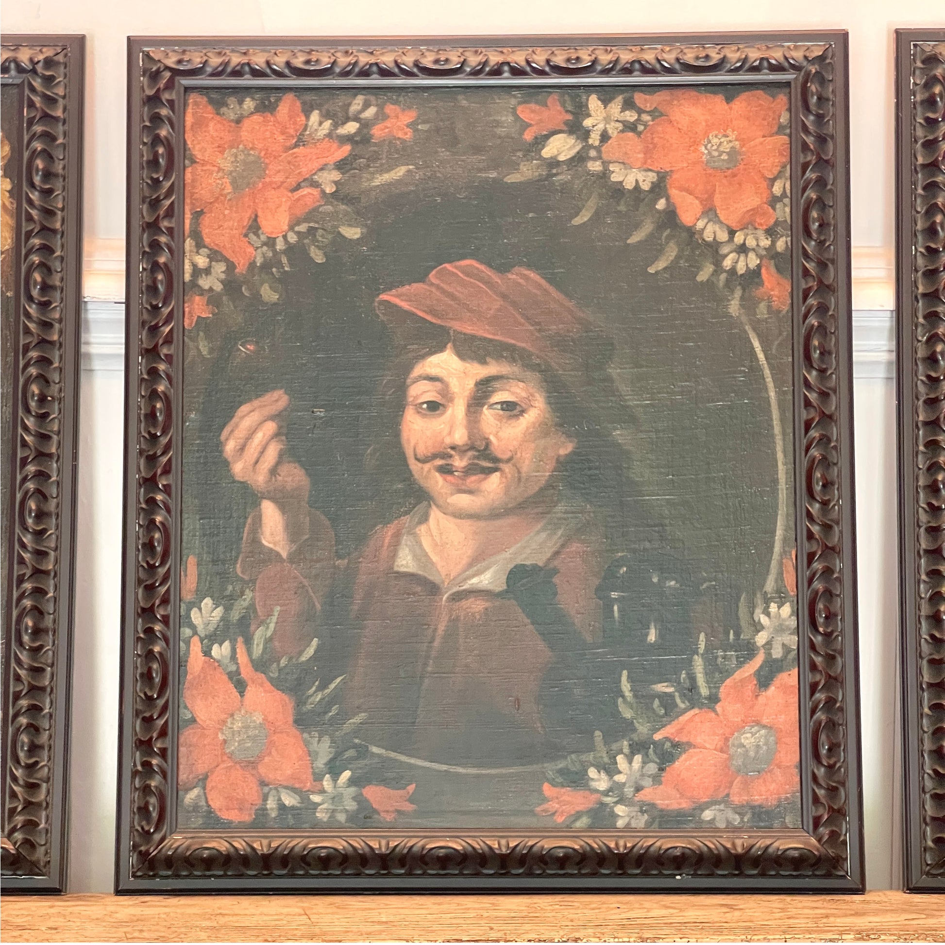 A framed antique oil painting depicting a man with a mustache holding a pipe surrounded by large orange flowers, housed in a dark carved wooden frame.