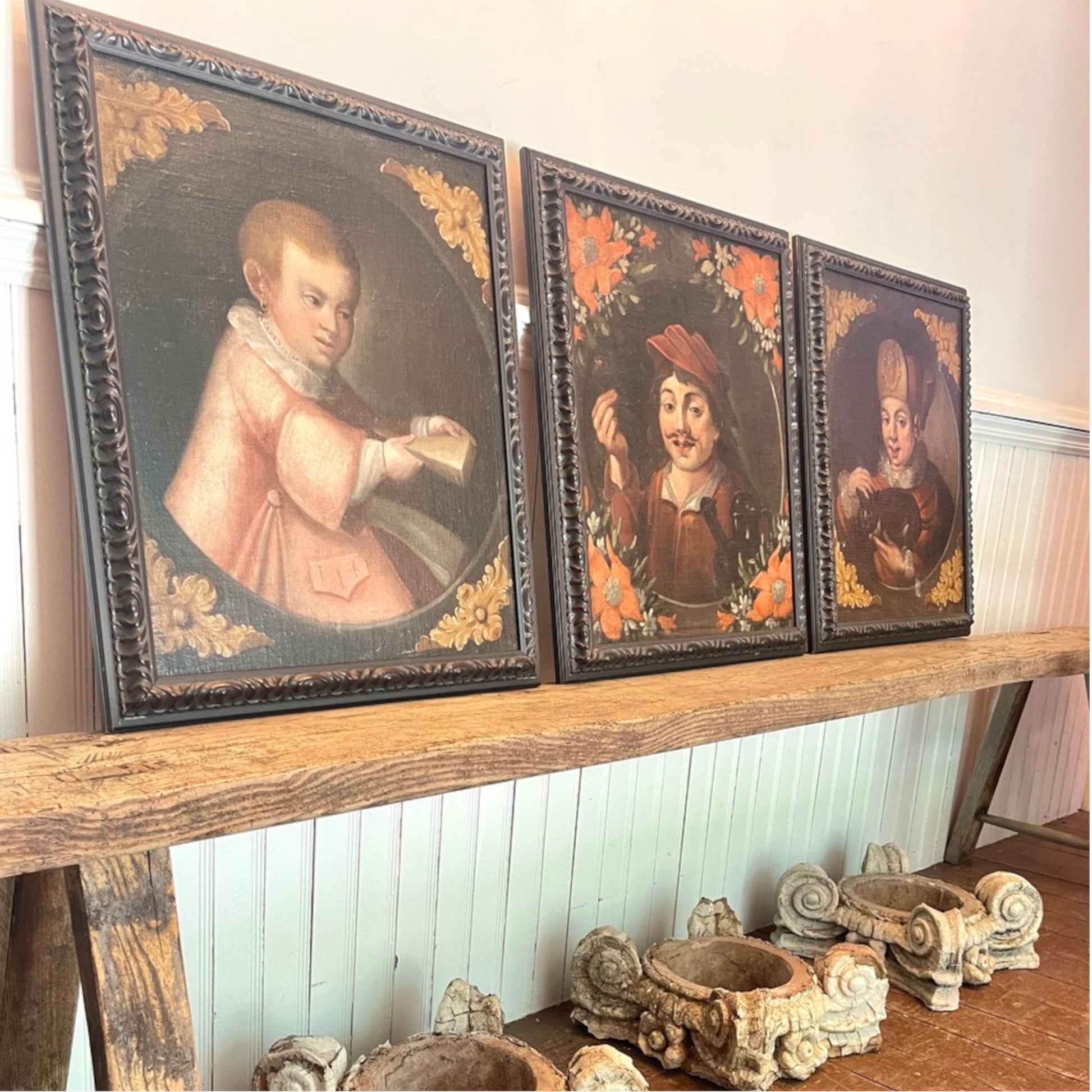 Three framed Old Masters oil portraits hanging on a wooden shelf against a white paneled wall.