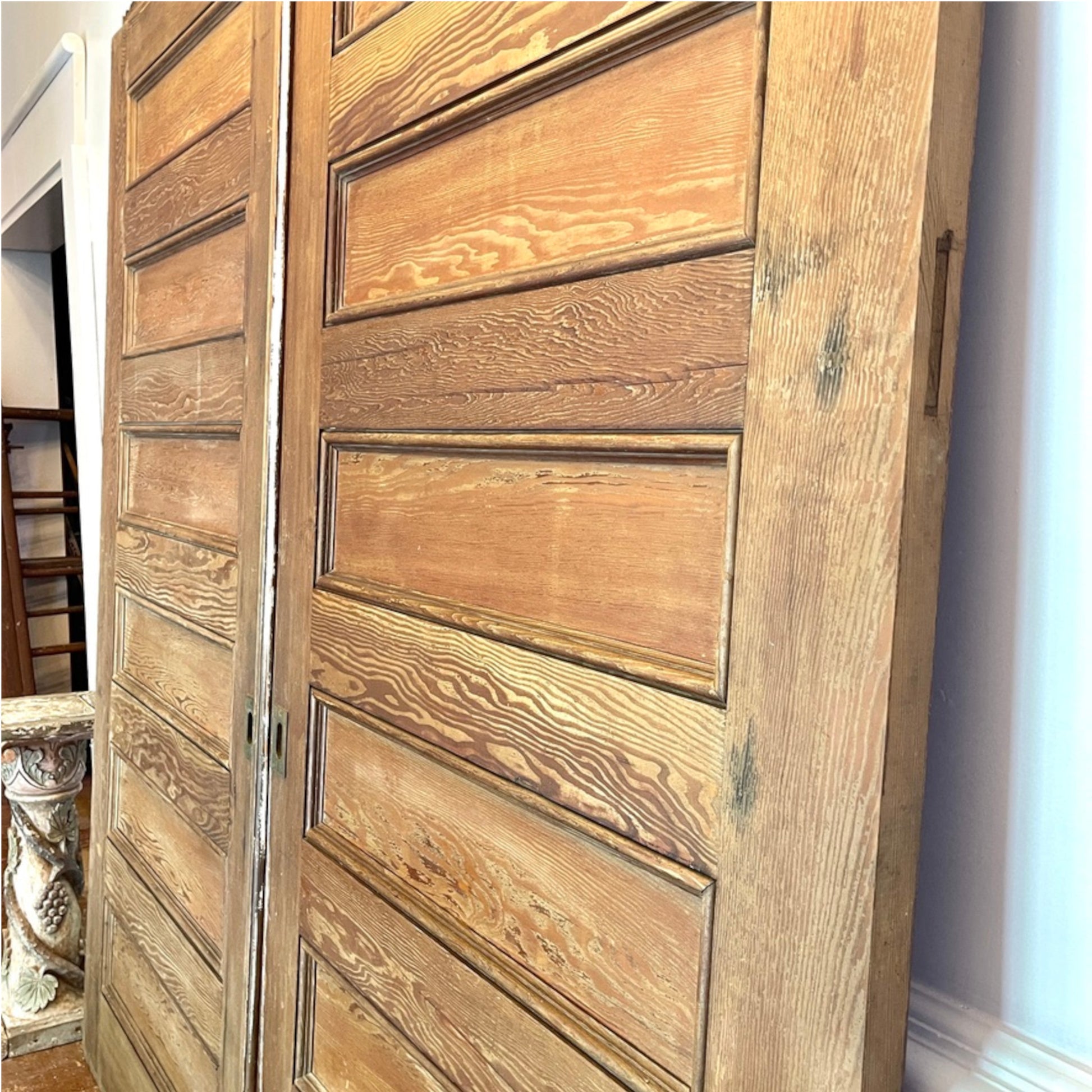 A pair of rustic, antique wooden interior doors with raised rectangular panels, showing warm medium-brown wood grain and natural knots.