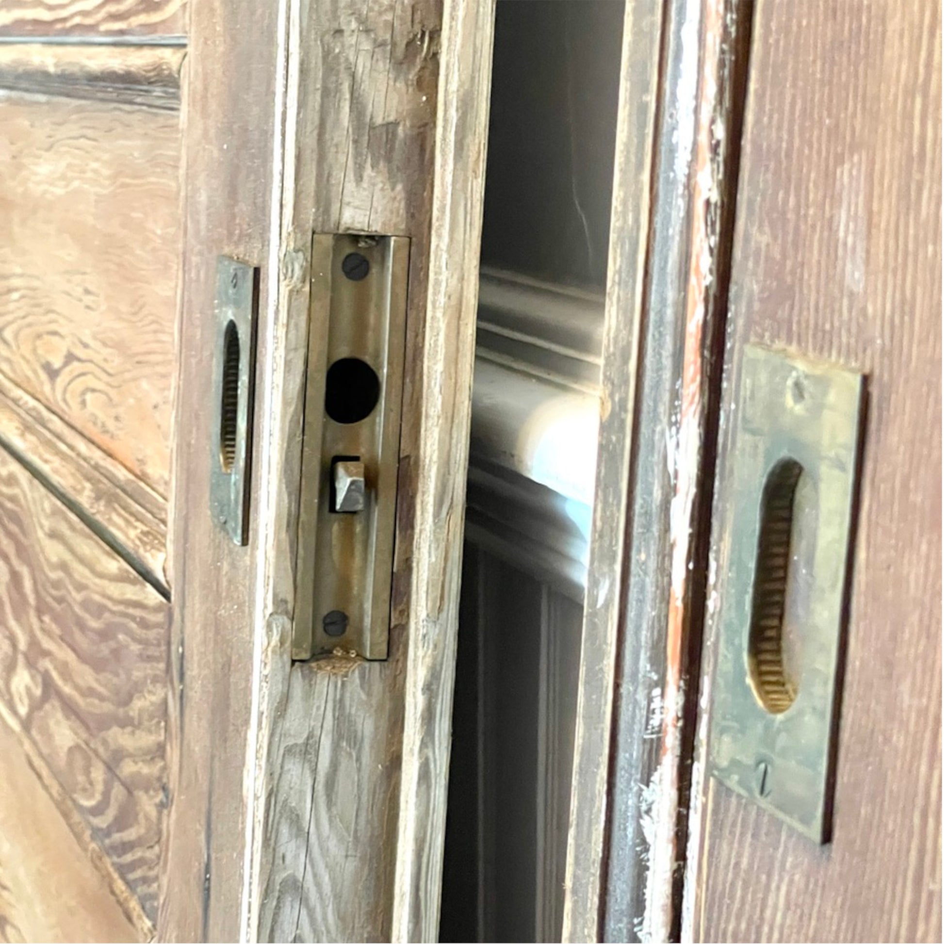 Close-up of weathered wooden doors with a metal latch mechanism and a brass-toned handle plate on the right side.