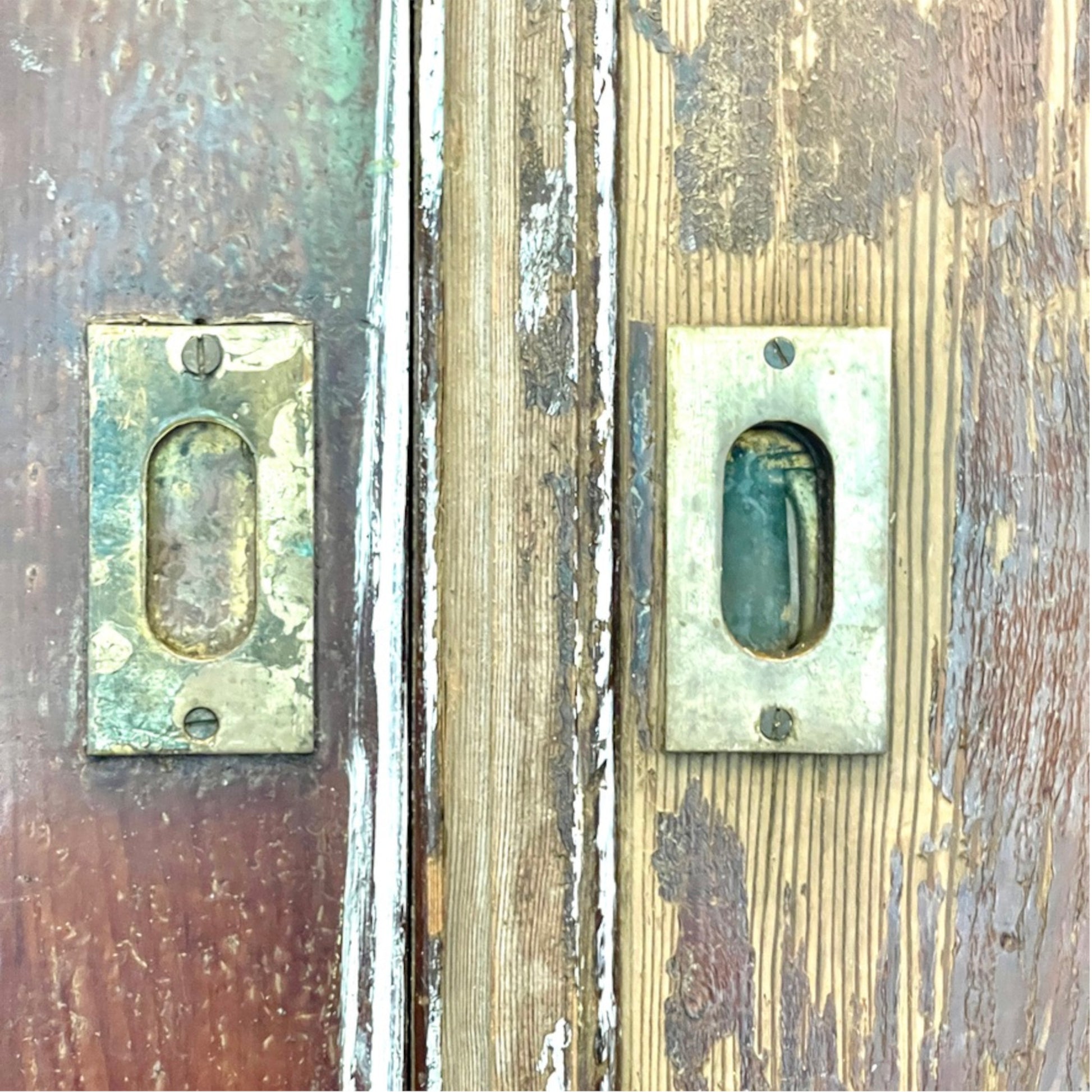 Distressed antique metal door hardware mounted on weathered wooden doors with peeling paint.