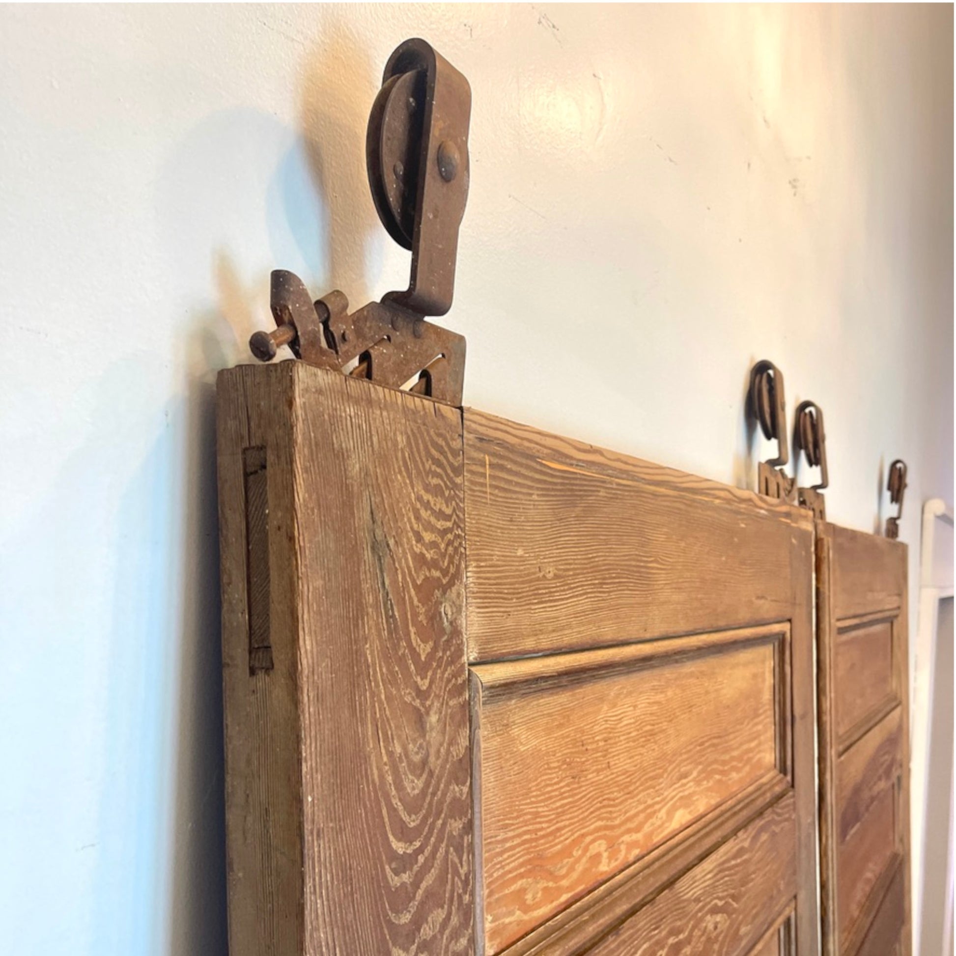 Close-up of a antique wooden pocekt doors with a dark metal pulley and bracket mounted above it, set against a plain off-white wall.
