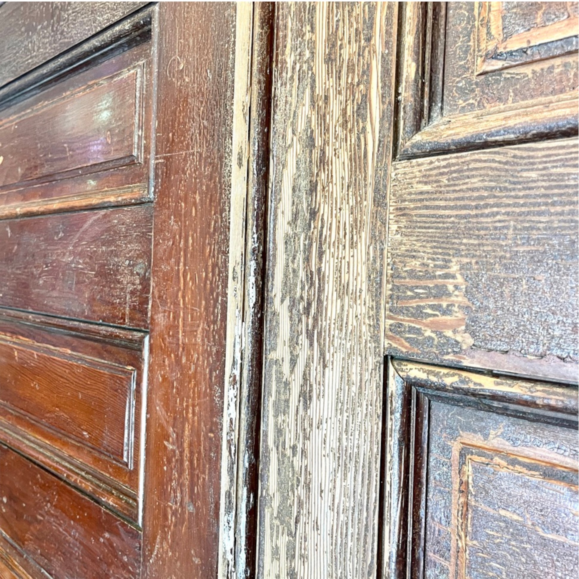 Close-up of a distressed wooden door with dark brown painted panels and a weathered, peeling light-colored finish showing the wood grain underneath.