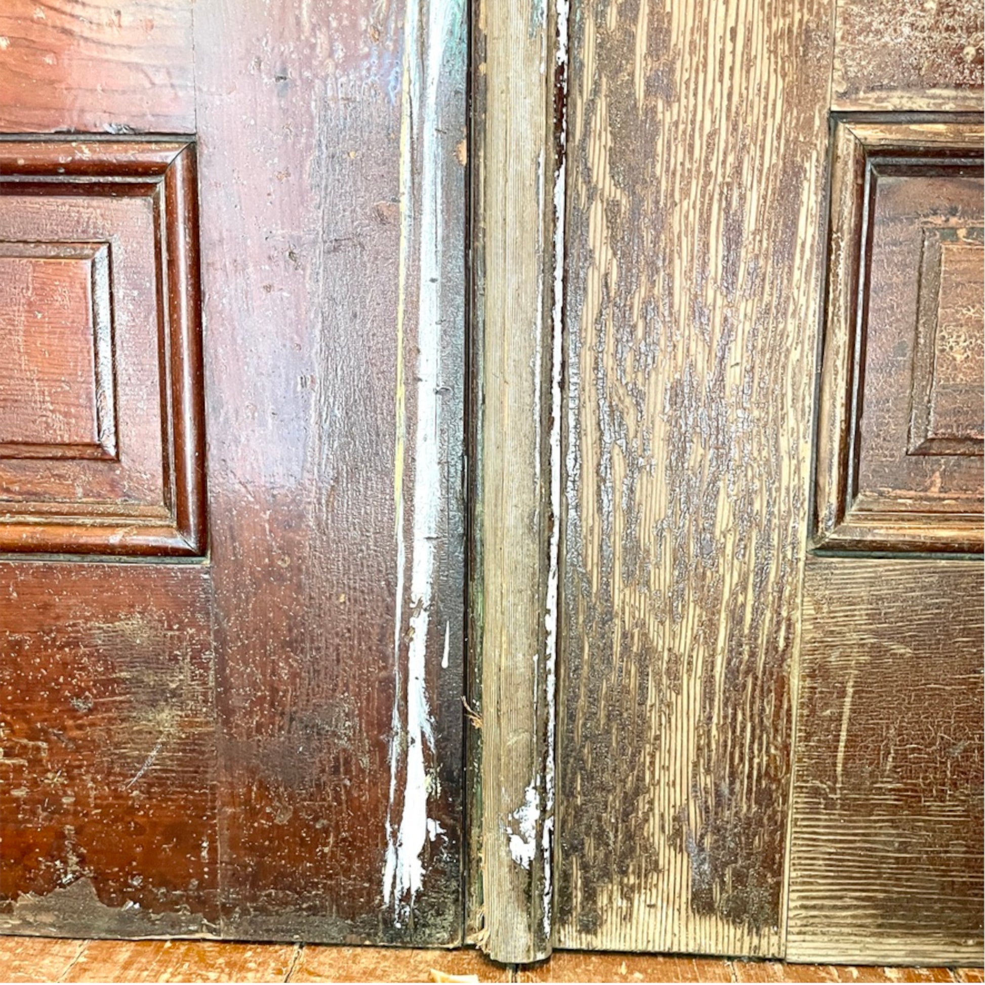 Close-up of weathered wooden doors with peeling paint and distressed brown wood grain, showing a close-up of the base of the doors.