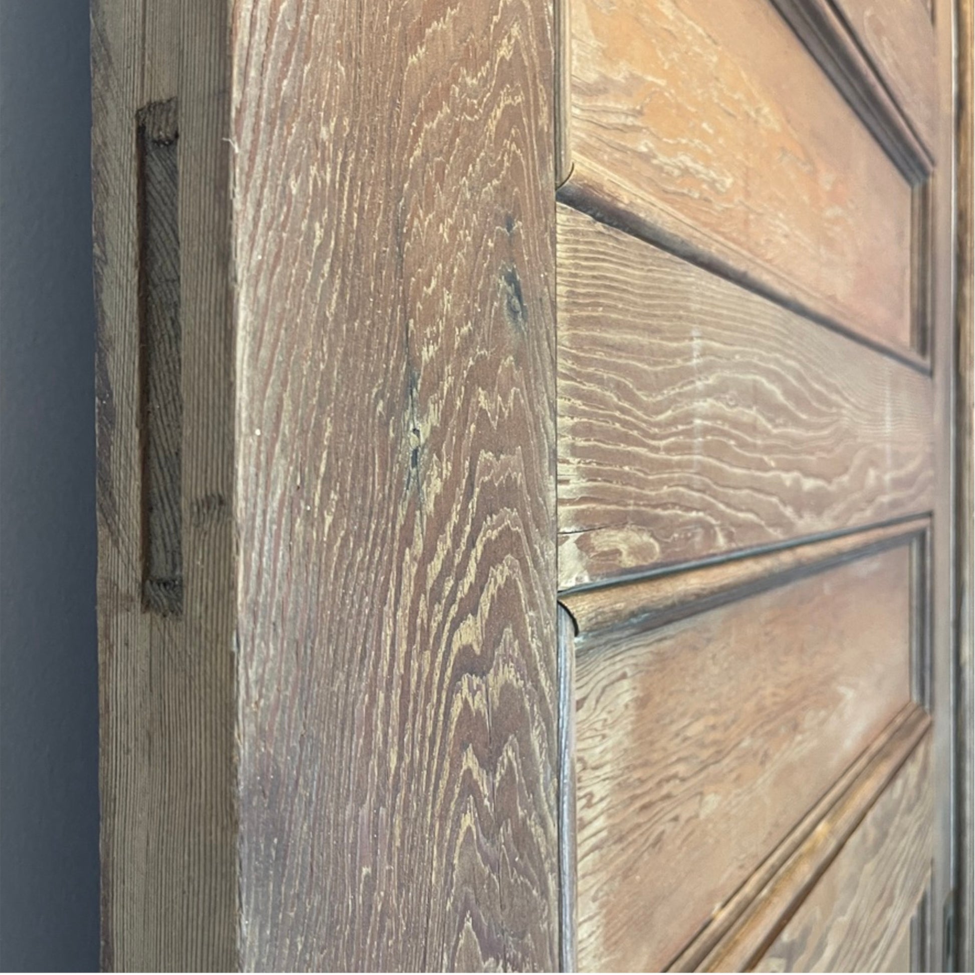 Close-up of a rustic wooden cabinet or door panel with a visible tongue-and-groove joint, showing natural wood grain.