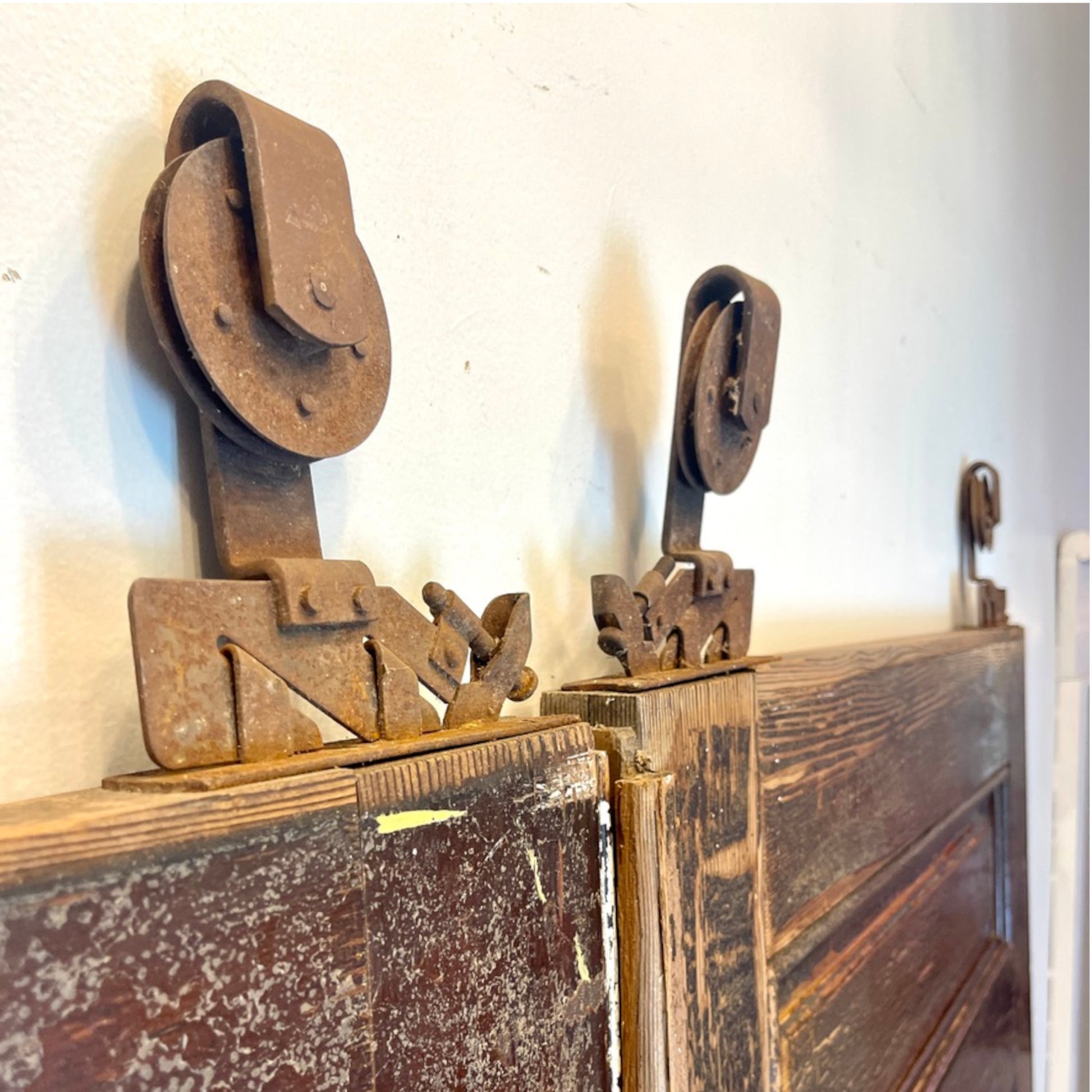 Rustic vintage metal pulley hardware mounted on a distressed wooden door against a white wall.
